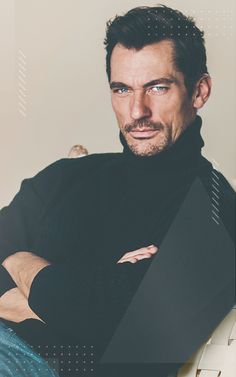 a man sitting down with his arms crossed and looking at the camera while wearing a black turtle neck sweater