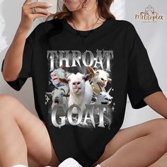 a woman sitting on the floor holding a cell phone and wearing a t - shirt with three goats printed on it