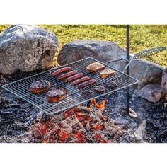 burgers and hamburger patties cooking on a grill in front of large rocks with flames