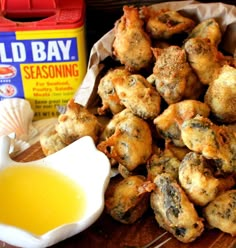 a pile of fried food sitting on top of a wooden cutting board next to a bottle of mustard