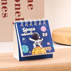 a small blue and white notebook with an astronaut on the cover, sitting on top of a wooden table