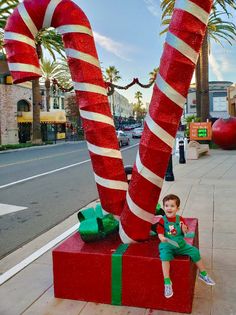 a young boy sitting on top of a red box next to giant candy canes