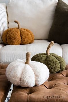 two white pumpkins sitting on top of a brown ottoman next to pillows and pillow covers