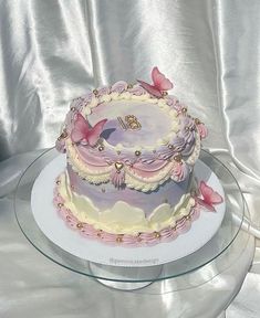 a pink and white cake with butterflies on it sitting on a glass platter next to a silver cloth