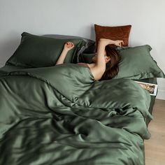 a woman laying in bed with green sheets and pillows