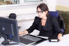 a woman sitting in front of a computer on a desk with a book next to her