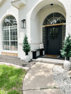 a white house with black front door and two planters on the sidewalk in front