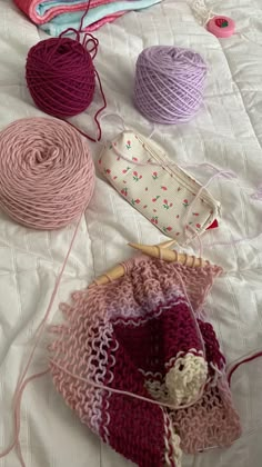 several balls of yarn sitting on top of a bed next to crochet hooks