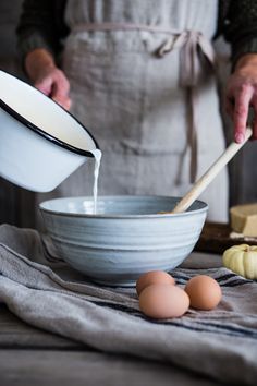 a person pouring milk into a bowl with eggs