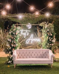 a couch sitting in the middle of a lush green field with lights strung above it