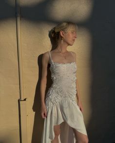 a woman in a white dress standing against a wall