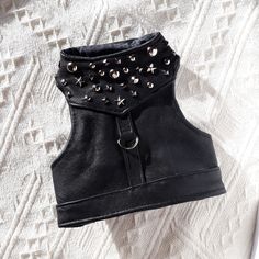 a black leather top with metal studs on the collar and side zipper, sitting on a white surface