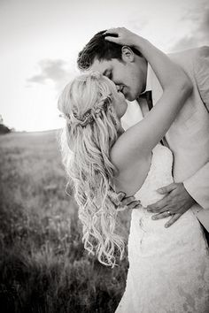 a bride and groom kissing in the middle of a field with tall grass behind them