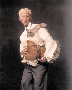 a young man wearing a white shirt and tie holding a brown bag with ruffles on it