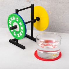 a small glass with water in it next to a toy weight and barbells