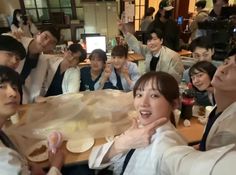 a group of people sitting around a table with food on it and one woman holding up her hand