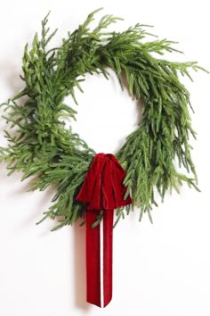 a christmas wreath with a red bow hanging from it's side on a white wall