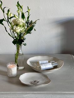 white flowers in a glass vase on a table next to two plates and a candle