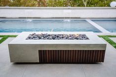 an outdoor fire pit in front of a swimming pool with grass and rocks around it