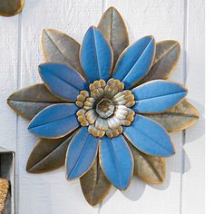 a blue and gold metal flower hanging on the side of a white wall next to a teddy bear