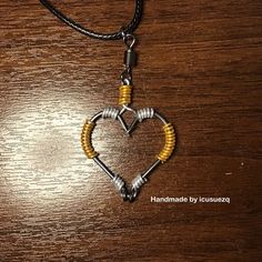 a heart shaped pendant with yellow beads on a wooden table next to a black cord