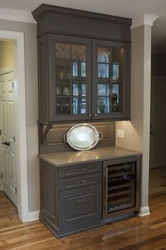 an empty kitchen with wooden floors and gray cupboards on the wall, along with a wine glass cabinet