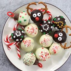 a white plate topped with chocolate covered pretzels and reindeer candies next to candy canes