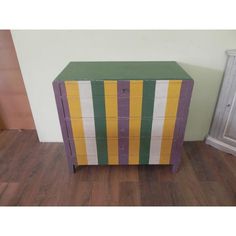 a multicolored chest of drawers sitting on top of a hard wood floor next to a white wall