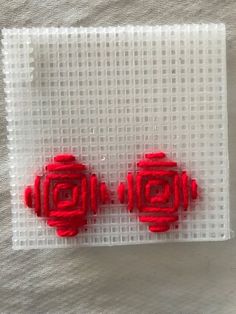 two red earrings sitting on top of a white piece of cloth next to each other