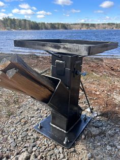 a metal object sitting on top of a rocky beach next to the ocean with trees in the background