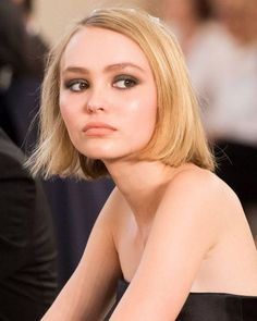 a woman with short blonde hair and black dress sitting in front of a man wearing a suit