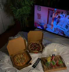 two pizzas sitting on top of a bed in front of a flat screen tv