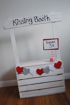 a sign that says kissing booth on top of a wooden crate with hearts hanging from it