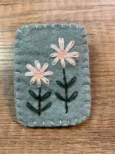 two flowers are embroidered onto the back of a small square piece of felt on a wooden table