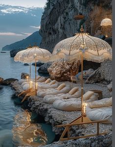 several umbrellas are set up on the rocks by the water at dusk with lights