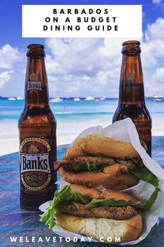 two beer bottles sitting next to each other on top of a table with sandwiches in front of them