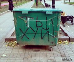 a green trash can sitting on the side of a road