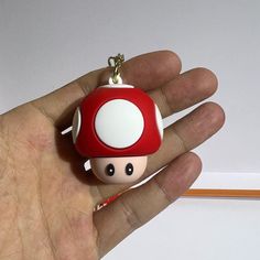 a hand holding a red and white mushroom keychain on it's thumb