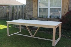 a wooden table sitting in the grass next to a house