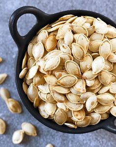 a black bowl filled with pumpkin seeds on top of a gray counter next to an orange peel