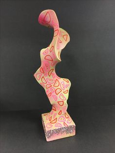 a pink and yellow sculpture with hearts on it's body, against a black background