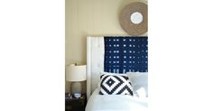 a white bed topped with a blue and white pillow next to a wall mounted clock