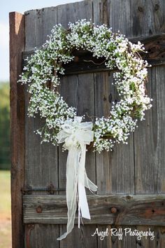 a white wreath with baby's breath hanging on an old wooden door in the country