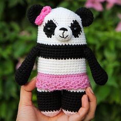 a crocheted panda bear in a pink and black outfit is held up by someone's hand