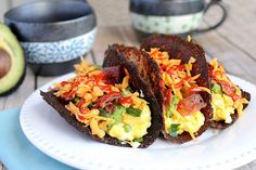 two pieces of toasted bread with eggs and vegetables on it sitting on a plate next to an avocado