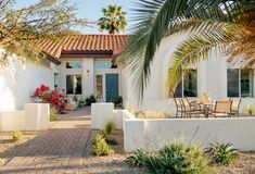 a white house with palm trees in the front yard and patio furniture on the outside