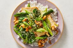 a purple plate topped with rice and veggies covered in sesame seed sauce on top of a white table