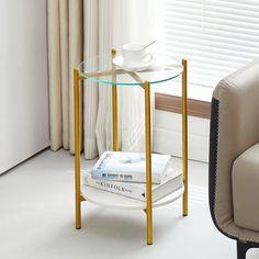 a glass table with books on it next to a chair and window in the background