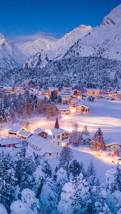 an aerial view of a town in the mountains at night with snow on the ground