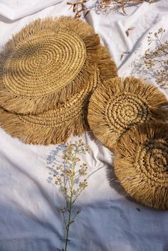 two straw hats sitting on top of a white sheet next to dried grass and flowers